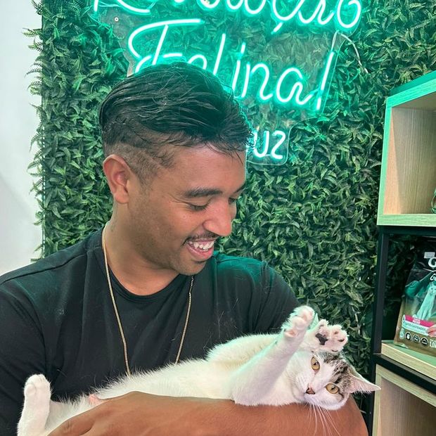 Profissional da Miauz com um gato no colo diante do letreiro Revolução Felina